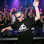 DJ with blue hair and sunglasses wearing DJing Is An Art oversized black t-shirt performing at nightclub