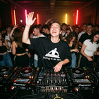 Female DJ wearing DJing Is An Art oversized t-shirt mixing on decks with energetic crowd under red lights