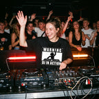 Female DJ wearing Warning DJ In Action Oversized T-Shirt performing in club hand raised