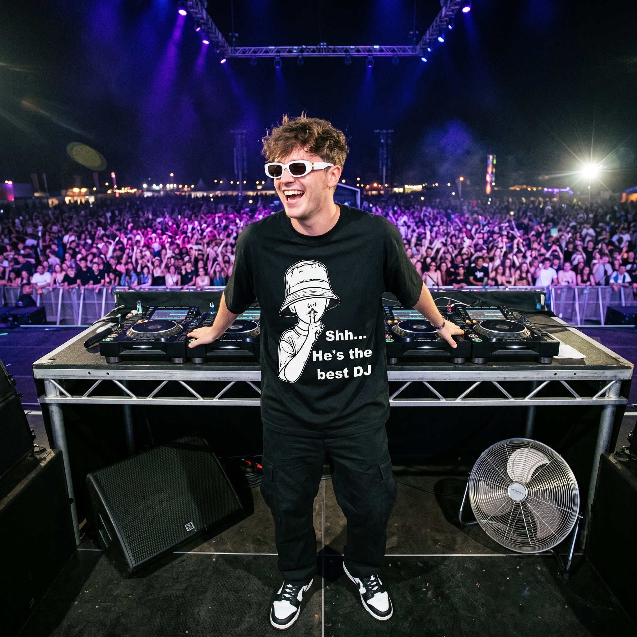 DJ in Shh He's The Best DJ oversized black t-shirt performing on outdoor festival stage in front of large crowd