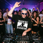 Male DJ wearing Warning DJ In Action Oversized T-Shirt in packed club blue hair sunglasses