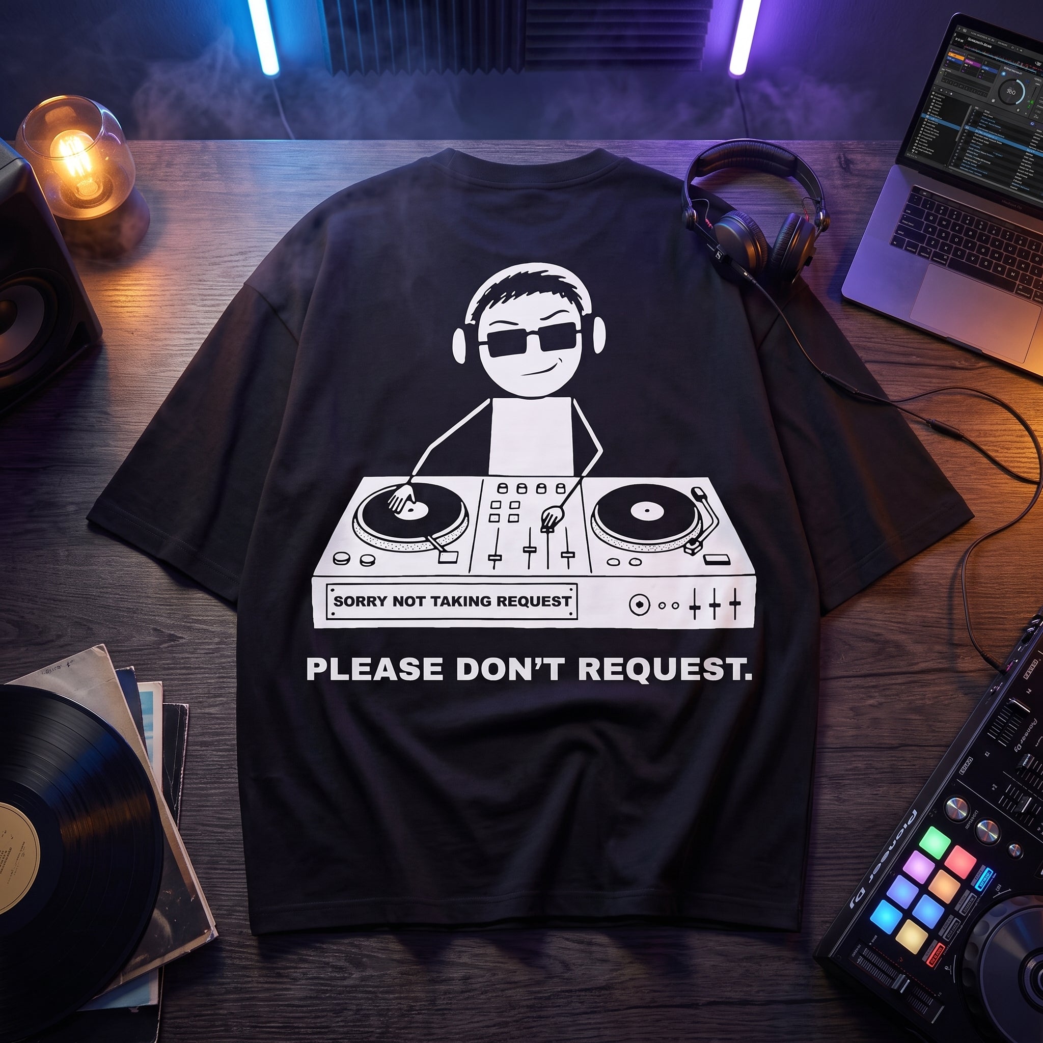 Black oversized t-shirt with Sorry Not Taking Request DJ graphic print, flat lay on wooden desk with turntables and vinyl records
