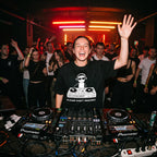 Female DJ wearing Sorry Not Taking Request oversized t-shirt mixing on decks with energetic crowd under red lights