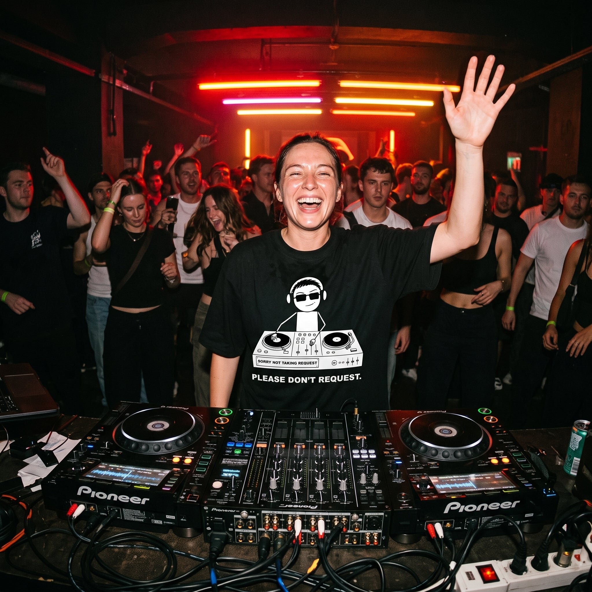 Female DJ wearing Sorry Not Taking Request oversized t-shirt mixing on decks with energetic crowd under red lights