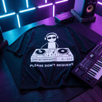 Black oversized DJ t-shirt with Please Don't Request graphic laid flat under neon blue and purple studio lighting