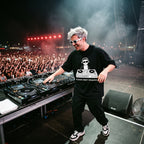 DJ in Please Don't Request oversized black t-shirt performing on outdoor festival stage in front of large crowd