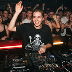 Female DJ wearing skeleton DJ graphic oversized t-shirt mixing on decks with energetic crowd under red lights