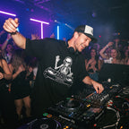 DJ wearing skeleton DJ graphic oversized t-shirt performing on Pioneer decks in front of cheering club crowd