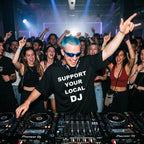 DJ with blue hair and sunglasses wearing Support Your Local DJ black oversized t-shirt performing live with arms raised