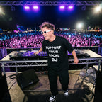 DJ in Support Your Local DJ oversized black t-shirt performing on outdoor festival stage in front of large crowd