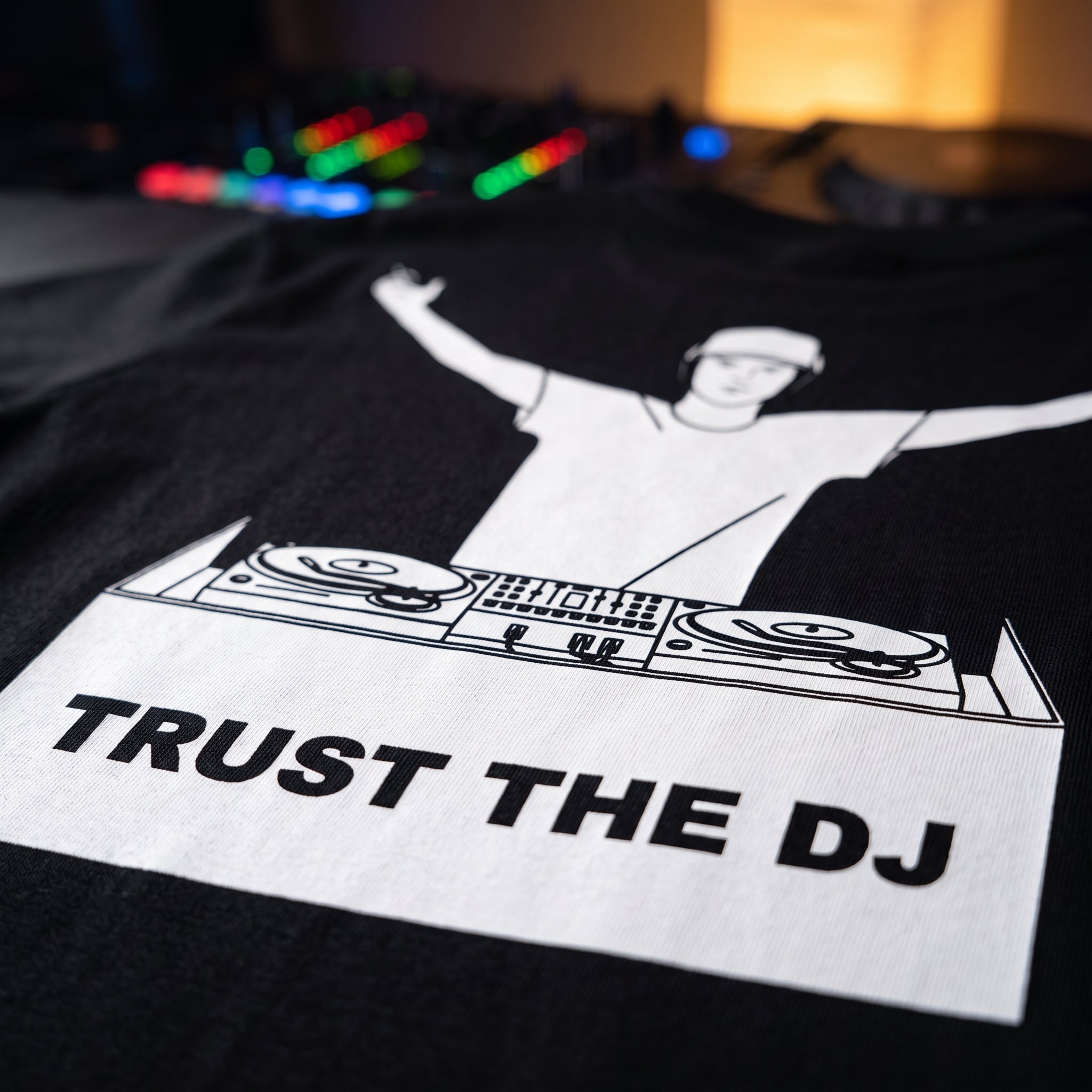 Close up print detail of Trust The DJ Quote Black Oversized T-Shirt DJ controller background