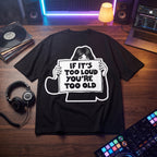 Black oversized t-shirt with If It's Too Loud You're Too Old graphic print, flat lay on wooden desk with vinyl records and DJ controller