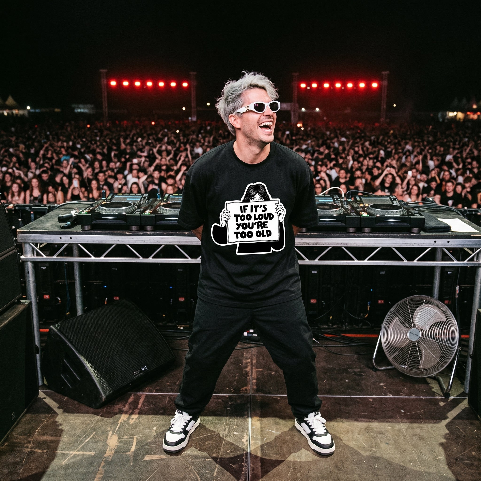 DJ in If It's Too Loud You're Too Old oversized black t-shirt performing on outdoor festival stage in front of large crowd