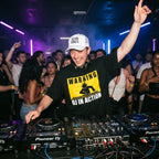 DJ wearing Warning DJ In Action oversized t-shirt performing on Pioneer decks in front of cheering club crowd