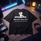 Black oversized t-shirt with World's Best DJ quote graphic, flat lay on wooden desk with DJ controller and vinyl records