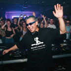 DJ with blue hair and sunglasses wearing World's Best DJ quote oversized black t-shirt performing at nightclub