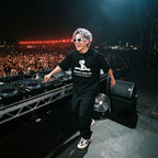 DJ in World's Best DJ quote oversized black t-shirt smiling at Pioneer decks on outdoor festival stage