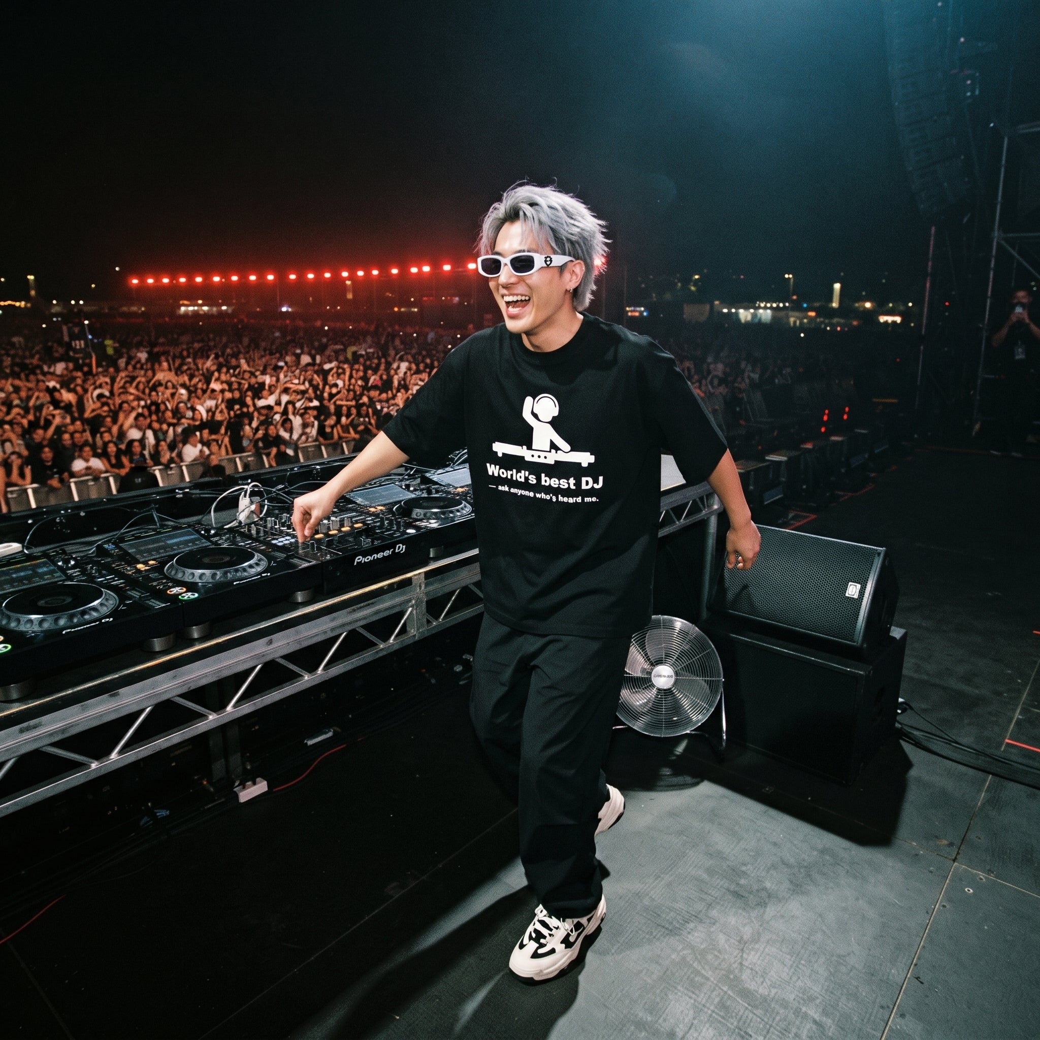 DJ in World's Best DJ quote oversized black t-shirt smiling at Pioneer decks on outdoor festival stage