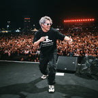DJ in World's Best DJ quote oversized black t-shirt holding microphone on outdoor festival stage in front of large crowd