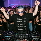 Male DJ wearing BPM Chart Oversized T-Shirt performing in packed club hands raised