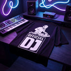 Premium black Official DJ Oversized T-Shirt laid on studio desk with synthesizer keyboard and neon lighting