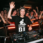 Official DJ Oversized T-Shirt worn by female DJ with headphones mixing tracks on Pioneer DJ console at club event